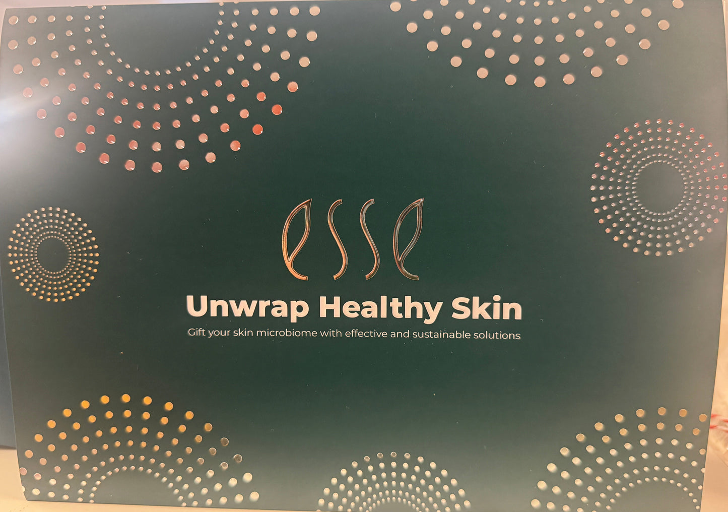 En grønn eske med gull- og hvitprikkete sirkler, med Hudkonsulenten Monrad-Krohns Esse Trial/Travel Pack Sensitive skin - oppdag produkter for sensitiv hud og gi mikrobiomet ditt effektiv og bærekraftig pleie.