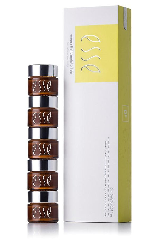 Fem små brune krukker med sølvfargede lokk står ved siden av en høy, hvit og grønngul eske merket Esse Omega Light Moisturiser 5X10Ml fra Hudkonsulenten Monrad-Krohn, med prebiotika hudpleie og en matt finish for frisk hud.
